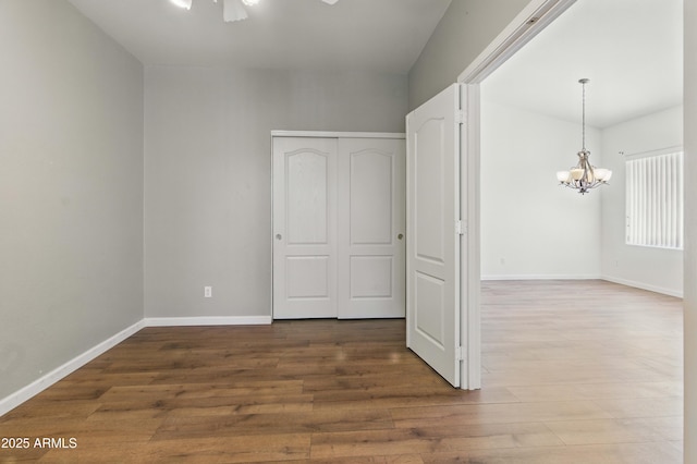 unfurnished room featuring a chandelier, wood finished floors, and baseboards