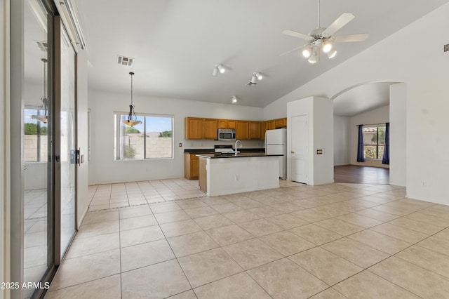 kitchen with freestanding refrigerator, stainless steel microwave, dark countertops, open floor plan, and arched walkways