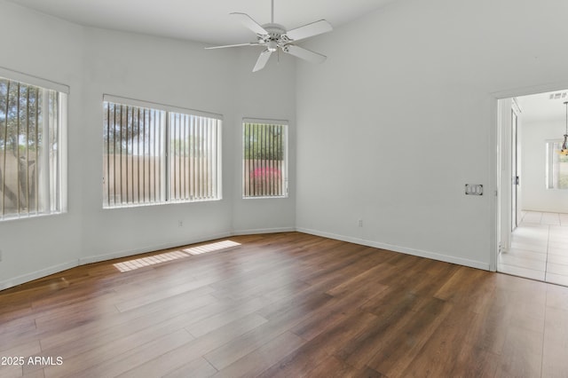 empty room featuring a ceiling fan, wood finished floors, baseboards, and high vaulted ceiling