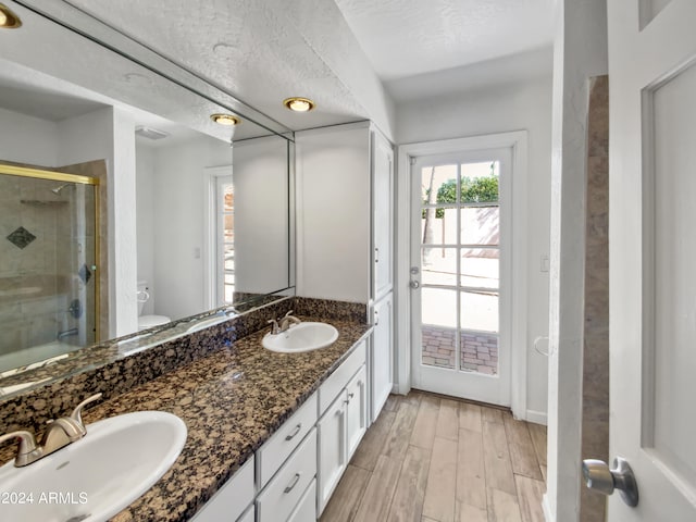 bathroom with vanity, a textured ceiling, hardwood / wood-style flooring, a shower with door, and toilet