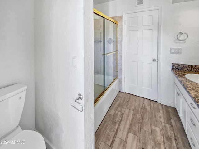 full bathroom featuring wood-type flooring, combined bath / shower with glass door, vanity, and toilet