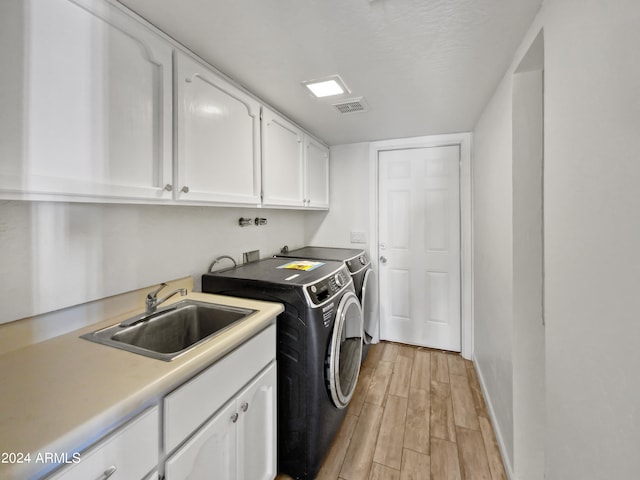 clothes washing area featuring cabinets, separate washer and dryer, sink, and light hardwood / wood-style floors