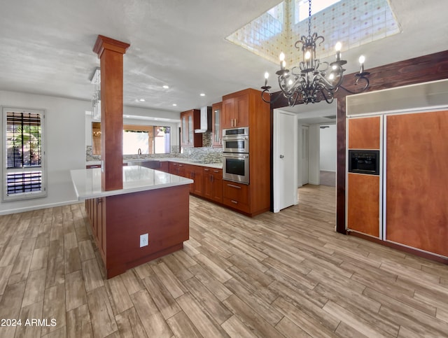 kitchen with light hardwood / wood-style floors, wall chimney range hood, decorative light fixtures, double oven, and ornate columns