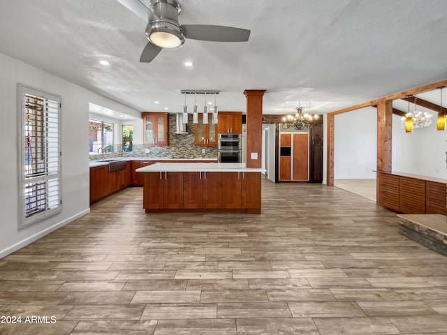 kitchen featuring light hardwood / wood-style floors, a kitchen island, wall chimney range hood, decorative light fixtures, and double oven