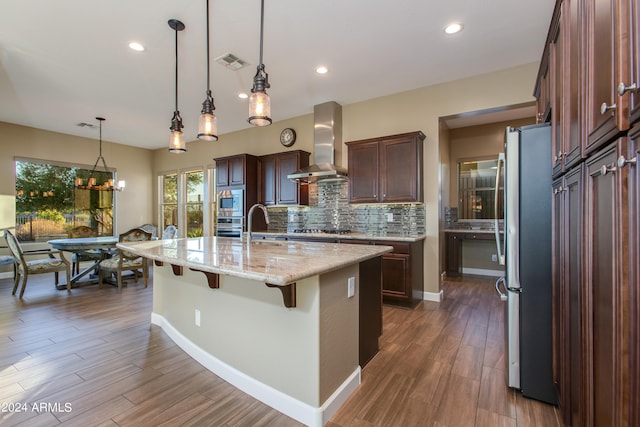 kitchen featuring an island with sink, light stone countertops, dark wood-type flooring, wall chimney exhaust hood, and stainless steel appliances