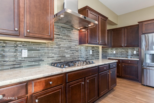 kitchen featuring wall chimney range hood, backsplash, light hardwood / wood-style floors, stainless steel appliances, and light stone counters