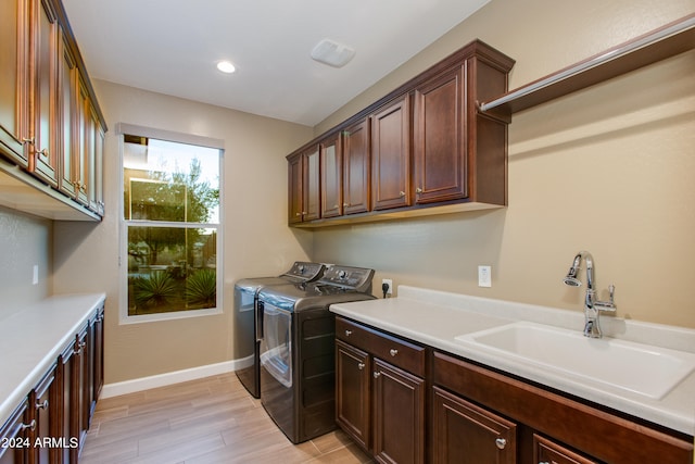 laundry area featuring sink, light hardwood / wood-style flooring, washing machine and dryer, and cabinets