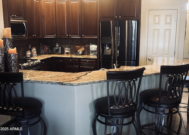 14000 N 94th St Unit 1077, Scottsdale, AZ 85260 - kitchen with stainless steel appliances, light stone counters, decorative backsplash, a breakfast bar area, and dark brown cabinets