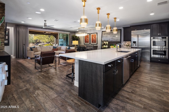 kitchen featuring pendant lighting, an island with sink, sink, stainless steel appliances, and dark wood-type flooring