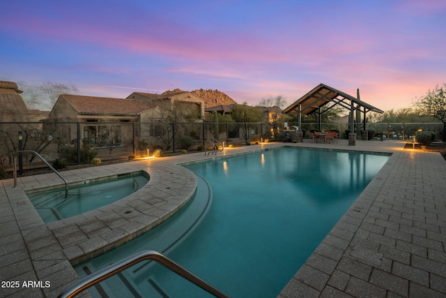 pool at dusk featuring an in ground hot tub, a gazebo, and a patio area