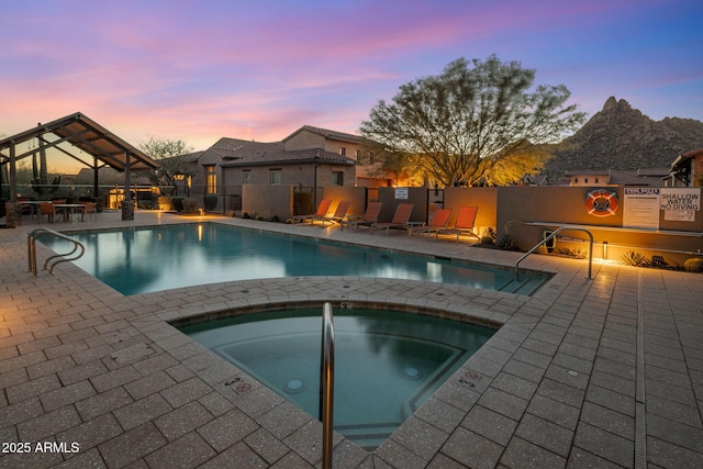 pool at dusk featuring a hot tub, a mountain view, and a patio area