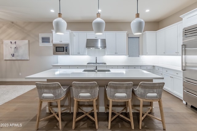 kitchen featuring appliances with stainless steel finishes, decorative light fixtures, a center island with sink, and range hood