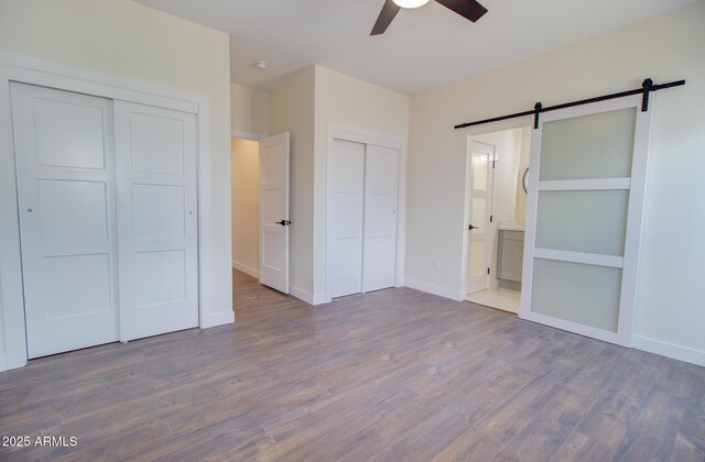 4115 N Monarch Dr, Eloy, AZ 85131 - unfurnished bedroom featuring multiple closets, a barn door, wood finished floors, and baseboards