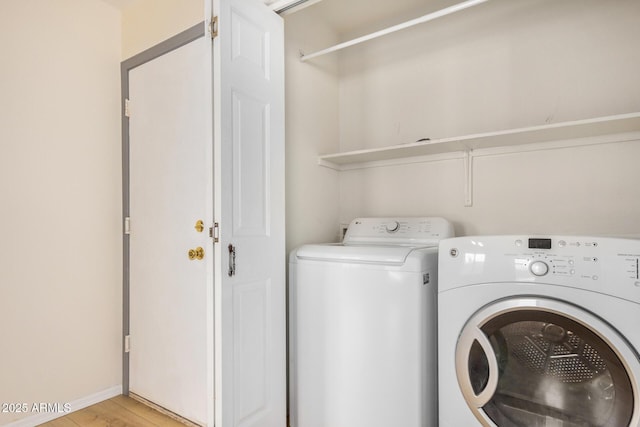 clothes washing area with laundry area, washing machine and dryer, and light wood finished floors