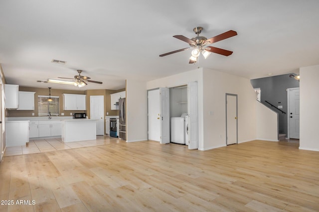 unfurnished living room with baseboards, washing machine and dryer, light wood-style floors, a ceiling fan, and a sink