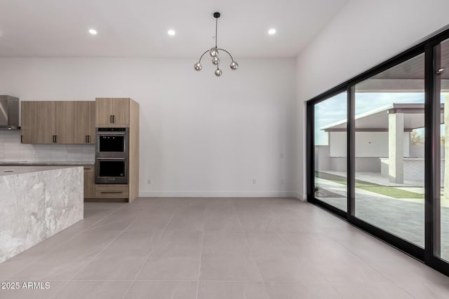 kitchen featuring double oven, tasteful backsplash, a notable chandelier, decorative light fixtures, and wall chimney exhaust hood