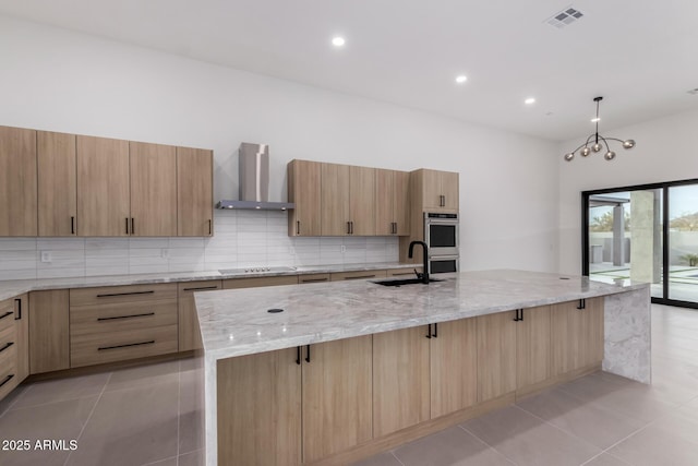 kitchen featuring a large island, wall chimney range hood, sink, light stone counters, and decorative backsplash