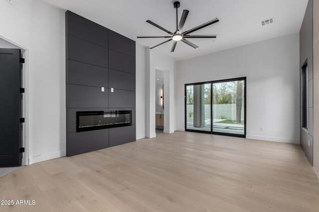 unfurnished living room with light hardwood / wood-style floors, a large fireplace, and ceiling fan