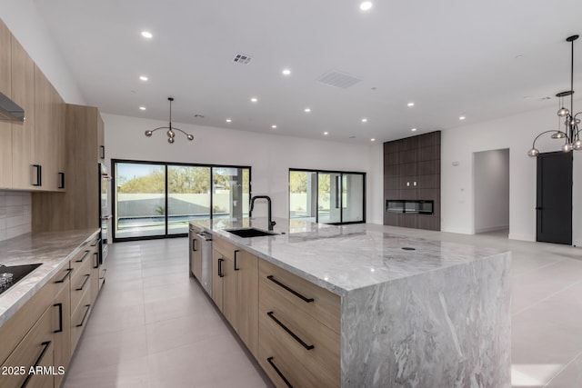 kitchen featuring sink, hanging light fixtures, light stone counters, tasteful backsplash, and a large island with sink