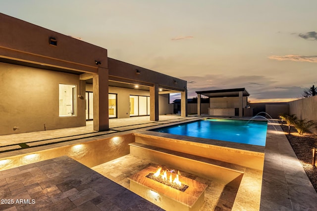 pool at dusk featuring a patio, a fire pit, and pool water feature