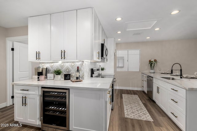 kitchen with tasteful backsplash, white cabinets, wine cooler, appliances with stainless steel finishes, and a sink