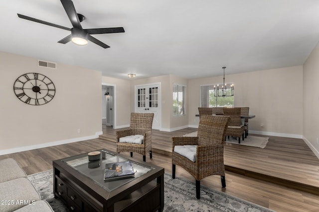 living area with visible vents, baseboards, ceiling fan with notable chandelier, and wood finished floors