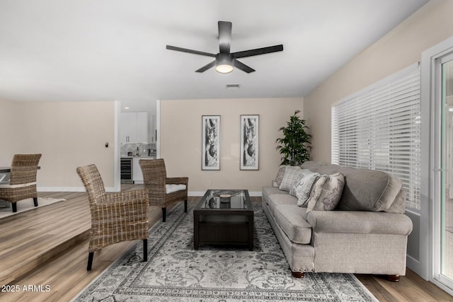 living room featuring visible vents, baseboards, a ceiling fan, wine cooler, and light wood finished floors