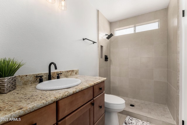 bathroom with tile patterned floors, toilet, tiled shower, and vanity