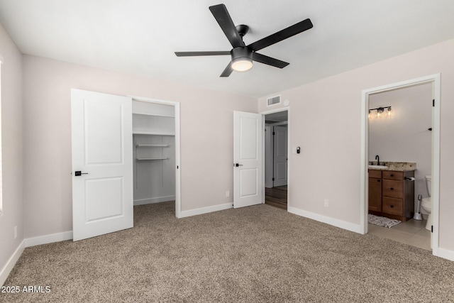 unfurnished bedroom with a closet, light colored carpet, visible vents, a sink, and a walk in closet