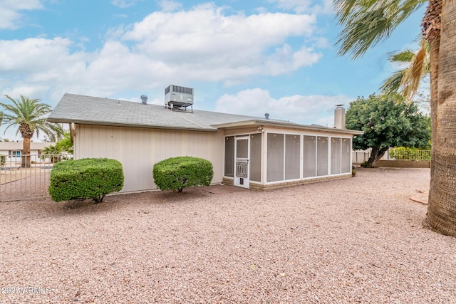 rear view of property with a sunroom, a chimney, fence, and central AC