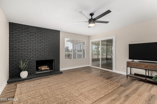 living area with a brick fireplace, baseboards, wood finished floors, and ceiling fan