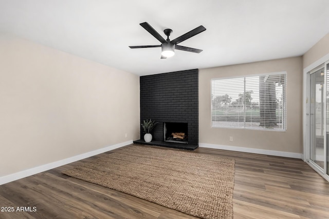 unfurnished living room featuring baseboards, a ceiling fan, wood finished floors, and a fireplace