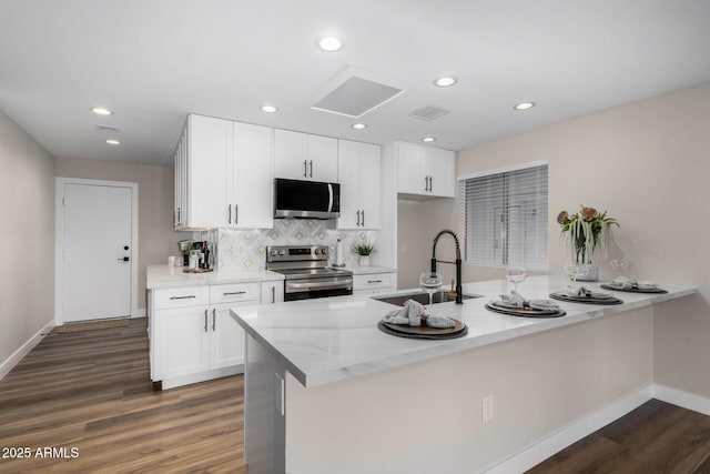 kitchen with a peninsula, white cabinetry, backsplash, appliances with stainless steel finishes, and a sink