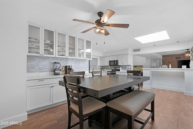 dining space featuring ceiling fan, baseboards, wood finished floors, a skylight, and visible vents