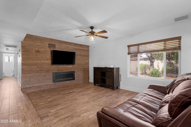 living room featuring a ceiling fan, visible vents, a large fireplace, and light wood-style floors