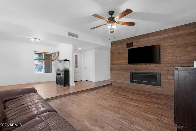 unfurnished living room featuring baseboards, ceiling fan, wood walls, and visible vents