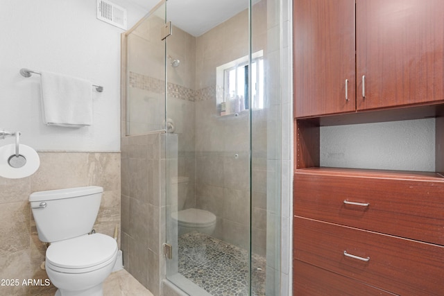 bathroom with tile walls, a stall shower, toilet, and visible vents