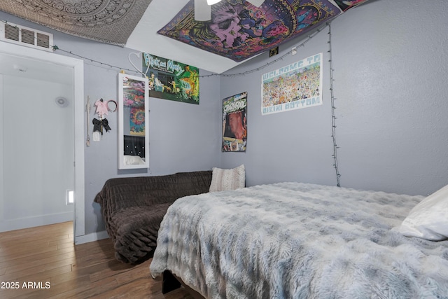 bedroom with baseboards, ceiling fan, wood finished floors, and visible vents