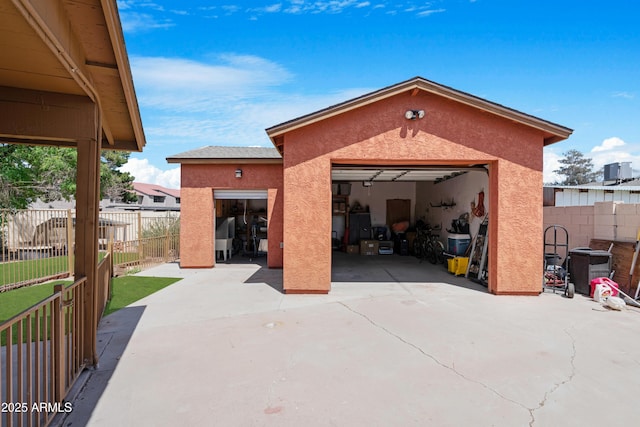 rear view of house featuring a detached garage, fence, an outbuilding, and stucco siding