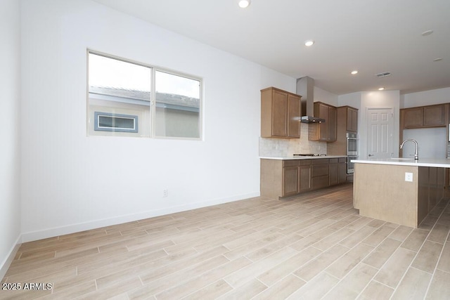 kitchen featuring cooktop, light countertops, wall chimney range hood, and visible vents