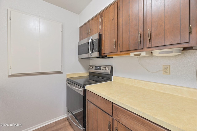 kitchen featuring baseboards, light countertops, appliances with stainless steel finishes, light wood-type flooring, and brown cabinets