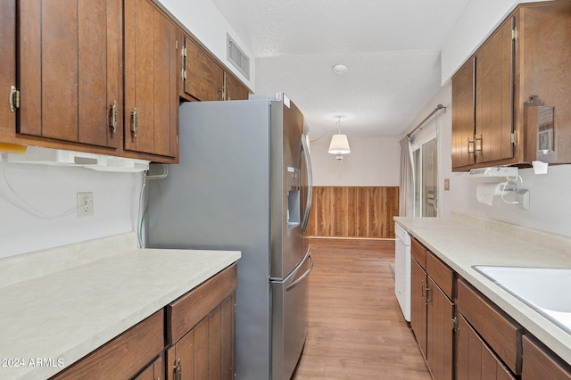 kitchen with light countertops, a wainscoted wall, stainless steel fridge, and visible vents