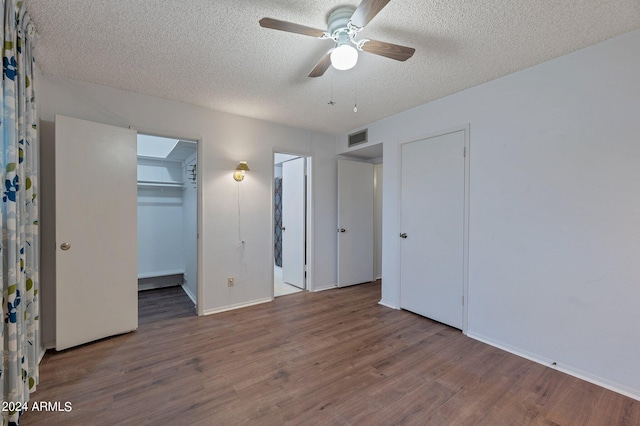 unfurnished bedroom featuring a textured ceiling, wood finished floors, visible vents, a ceiling fan, and a walk in closet