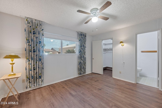 unfurnished bedroom with a closet, a spacious closet, ensuite bathroom, a textured ceiling, and wood finished floors