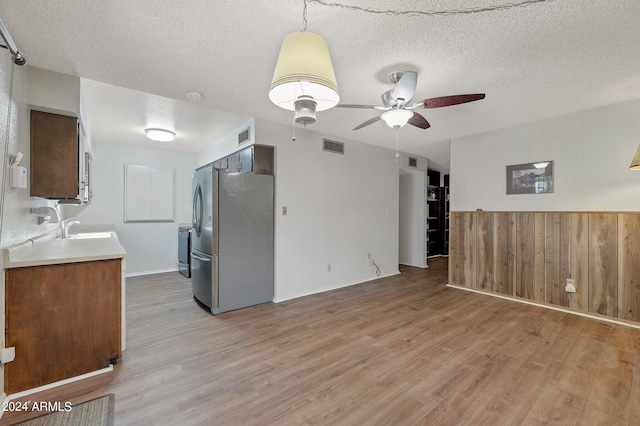 kitchen with light wood finished floors, freestanding refrigerator, light countertops, a textured ceiling, and a sink