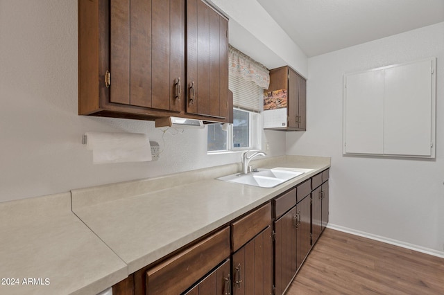 kitchen featuring light wood-style flooring, a sink, baseboards, light countertops, and dark brown cabinets