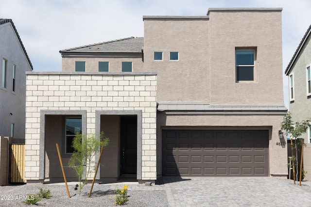 view of front facade with a garage, decorative driveway, fence, and stucco siding