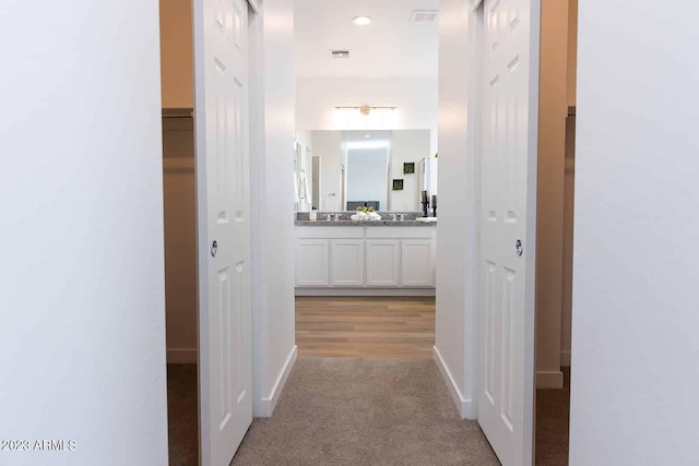 hallway featuring baseboards, visible vents, and light colored carpet