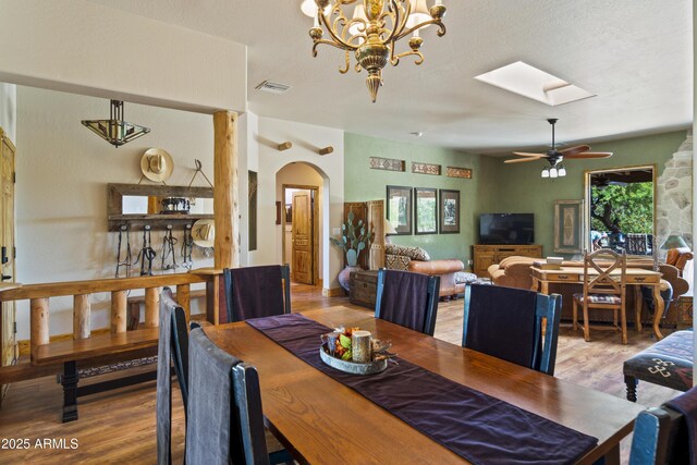 21909 W Beacon Ln, Wittmann, AZ 85361 - dining area with arched walkways, ceiling fan with notable chandelier, wood finished floors, a skylight, and visible vents