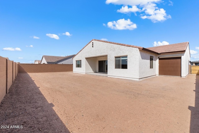 rear view of property with an attached garage, a fenced backyard, and stucco siding